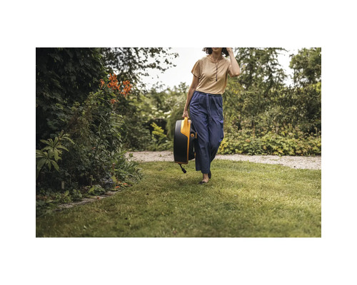 Femeie care poartă o cutie pentru furtun de grădină printr-o grădină.