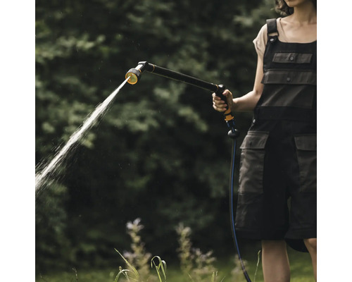 Femeie udând grădina cu un pistol de grădină pe un furtun de grădină.