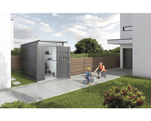 Magazie de grădină în grădină cu uși deschise, în care se pot vedea un scuter și unelte de grădină. O femeie ajută un copil să meargă pe bicicletă.