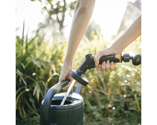 O persoană umple o stropitoare cu un furtun de grădină.