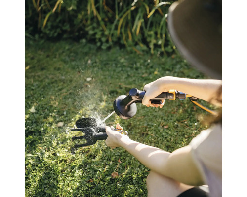 Proprietar de grădină care curăță unelte de grădină cu un furtun de grădină