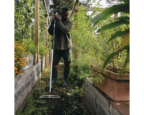 Bărbat în seră cu greblă de grădină pentru pregătirea solului.