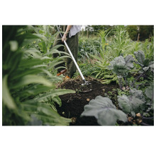 Scenă de grădină cu o persoană care folosește o sapă pentru a lucra pământul printre plante.