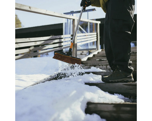 O persoană curăță zăpada de pe o scară cu o perie de zăpadă.