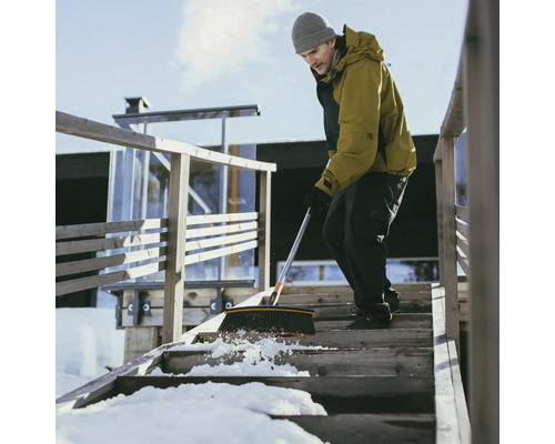 Un bărbat mătură zăpada cu o mătură de pe o scară de lemn din fața unei case.