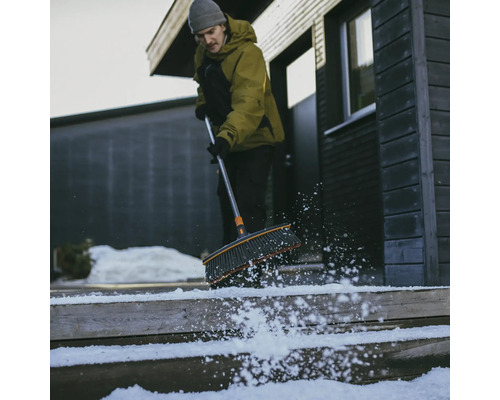 Bărbat măturând zăpada cu o mătură de pe o scară din fața unei case