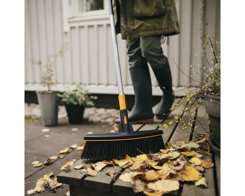 O persoană mătură frunze pe o terasă cu o mătură Fiskars.