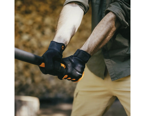 Un bărbat ține o unealtă cu mănuși de grădină negre marca Fiskars.