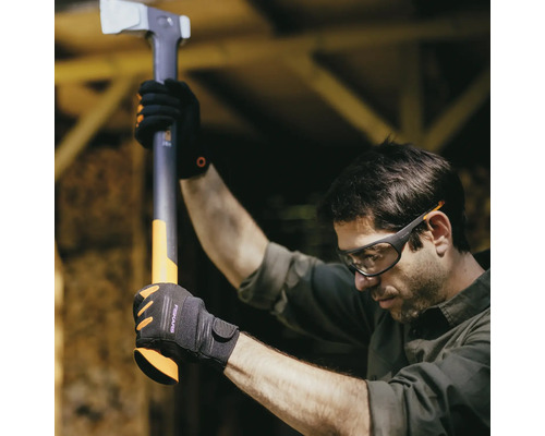 Bărbat cu ochelari de protecție și mănuși ține un topor de despicat Fiskars.
