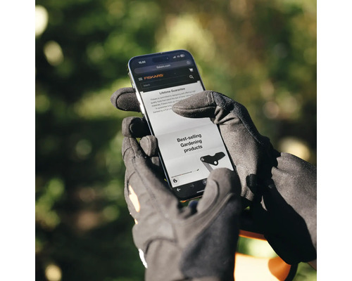 O persoană cu mănuși de grădinărit se uită la site-ul web Fiskars pe un smartphone.