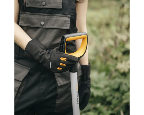 O persoană ține o lopată Fiskars în mână și poartă mănuși de grădinărit.