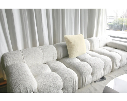 Canapea modulară cu pernă și structură tapițată în fața unei ferestre cu perdea