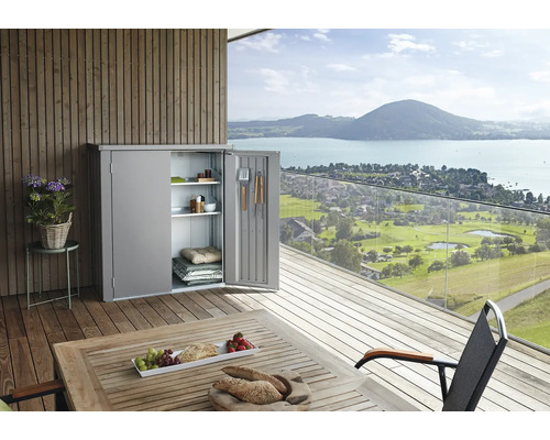 Dulap metalic de grădină cu ușa deschisă pe o terasă cu vedere la lac și la munte