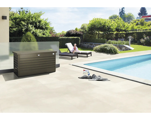 Scenă exterioară cu o cutie de depozitare lângă o piscină, șezlonguri și o grădină.