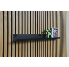 Raft negru de perete în fața unui perete cu lambriuri din lemn cu decorațiuni
