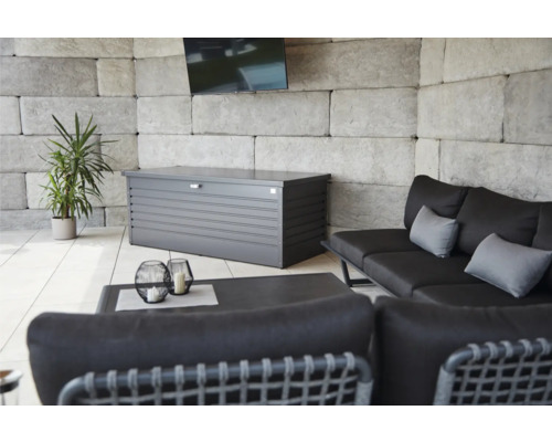 Spațiu exterior cu o cutie de depozitare gri, o canapea, o masă și o plantă.