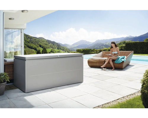 Ladă depozitare grădină Biohort LoungeBox 200 metal 200x84x88,5 cm 1400 l gri cuarț metalizat Scenă în aer liber cu o cutie mare de depozitare lângă o femeie așezată pe o canapea lângă o piscină, cu vedere la un peisaj montan