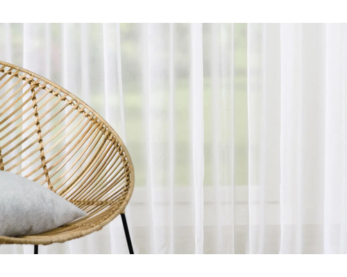 Scenă cu un scaun de ratan cu pernă și o perdea albă