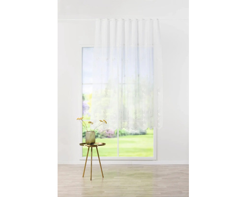 Perdea glisantă decorativă, transparentă, cu motiv floral, în fața unei ferestre într-o cameră luminoasă.