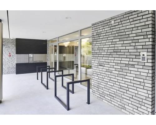 Zona de intrare a unei clădiri rezidențiale cu cutii poștale, suport pentru biciclete și un zid de cărămidă