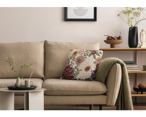 Scenă de living cu canapea bej, pernă decorativă florală și măsuță laterală