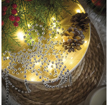 Decorare cu șirag de mărgele argintii, ramuri de brad și conuri de pin pe o masă rotundă.