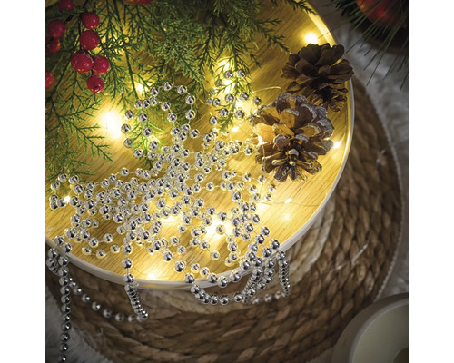 Decorare cu șirag de mărgele argintii, ramuri de brad și conuri de pin pe o masă rotundă.