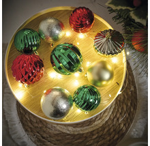 Globuri decorative de Crăciun în verde, roșu și auriu pe o tavă rotundă cu șir de lumini.