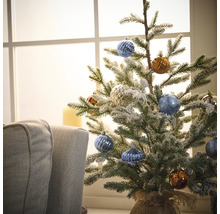 Brad mic de Crăciun decorat cu globuri în fața unei ferestre