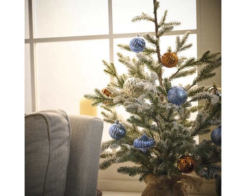 Brad mic de Crăciun decorat cu globuri în fața unei ferestre