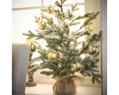 Brad decorativ de Crăciun, acoperit cu zăpadă, cu globuri aurii într-un sac de iută