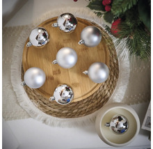 Globuri decorative de Crăciun argintii pe o farfurie de lemn și o masă