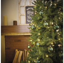 Brad împodobit cu luminițe și globuri în fața unui șemineu.