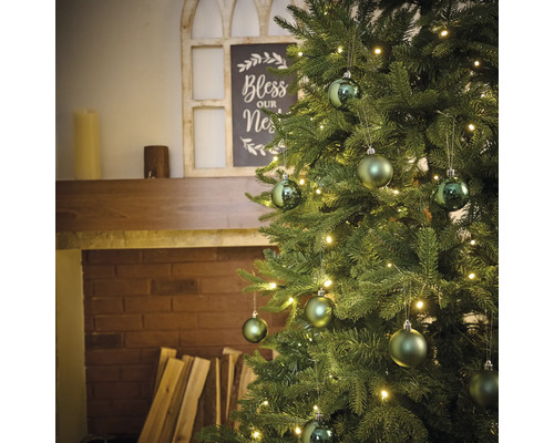 Brad împodobit cu luminițe și globuri în fața unui șemineu.