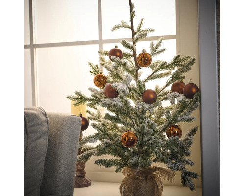 Brad împodobit, acoperit cu zăpadă, cu globuri maro într-un sac de iută