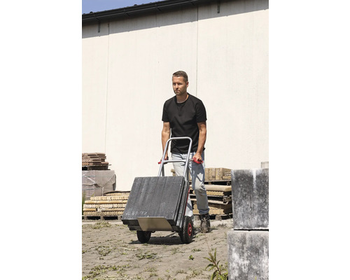 Un bărbat transportă pietre de pavaj cu un cărucior.