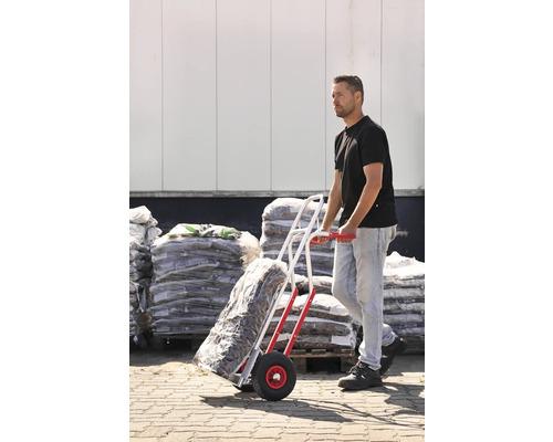 Bărbat transportă mărfuri în saci cu un cărucior în fața unui depozit