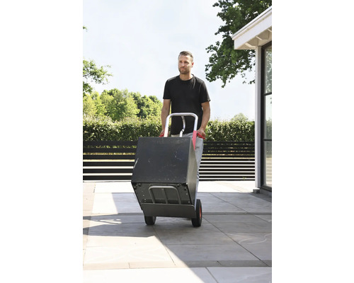 Bărbat transportând o cutie cu un cărucior de saci în aer liber.