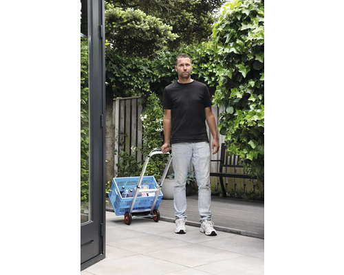 Un bărbat transportă o cutie albastră de cumpărături cu un cărucior în grădină
