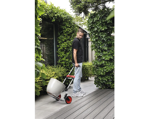 Bărbat transportă ghiveci de flori cu un cărucior în grădină.