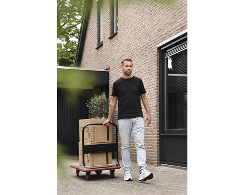 Un bărbat transportă cutii de mutare cu un cărucior de transport în fața unei case.