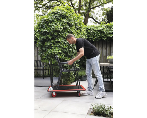 Bărbat transportând scaune pe o platformă rulantă în grădină