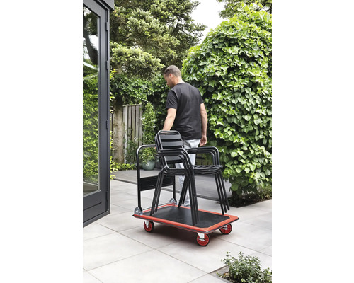 O persoană transportă scaune în grădină cu o scândură cu rotile.
