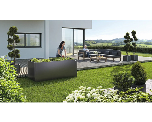 Scenă de grădină cu jardinieră înălțată, plantată de o femeie, și zonă de relaxare cu canapea și masă