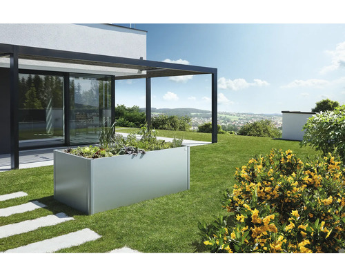 Jardinieră înaltă din metal în grădină cu plante și terasă adiacentă