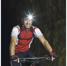Bărbat mergând cu bicicleta cu o lanternă frontală într-un tunel.
