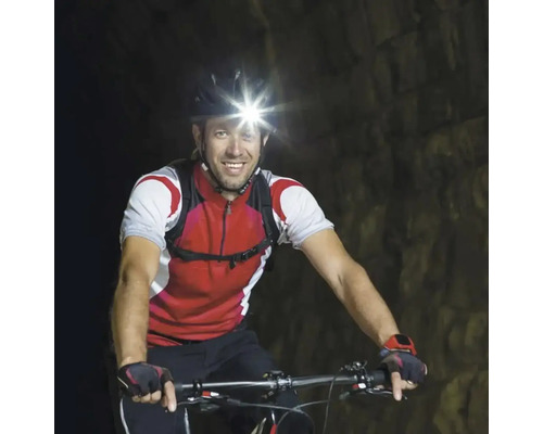 Bărbat mergând cu bicicleta cu o lanternă frontală într-un tunel.