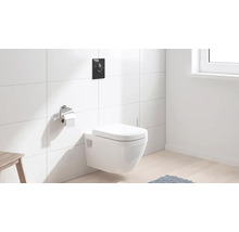 Vas WC suspendat cu placă de acționare și suport pentru hârtie igienică într-o baie cu faianță albă.