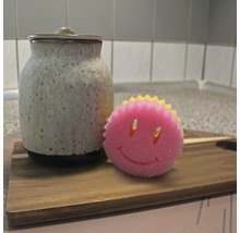 Recipient ceramic cu capac și un burete de spălat vase cu față zâmbitoare pe o scândură de lemn