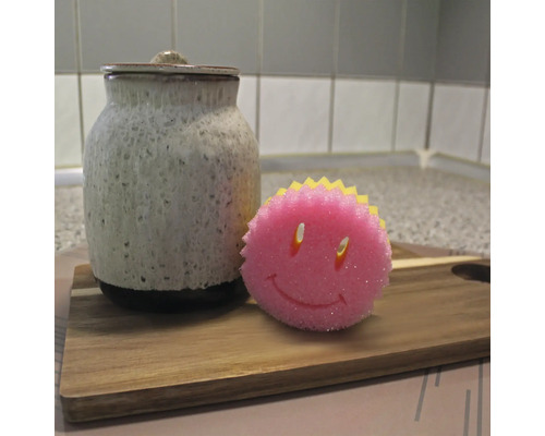 Recipient ceramic cu capac și un burete de spălat vase cu față zâmbitoare pe o scândură de lemn